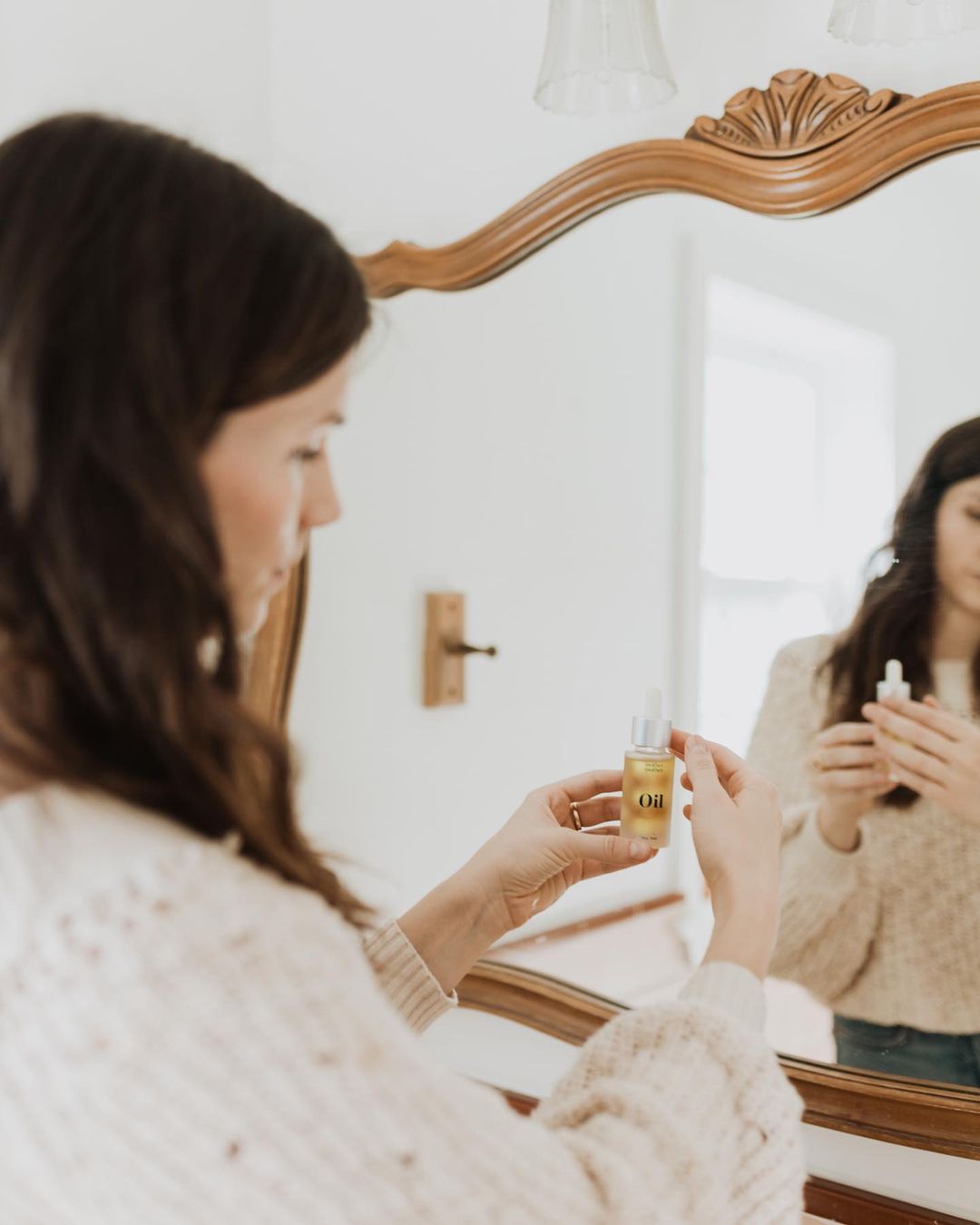 woman standing in front of a mirror holding  Mother Mother Oil