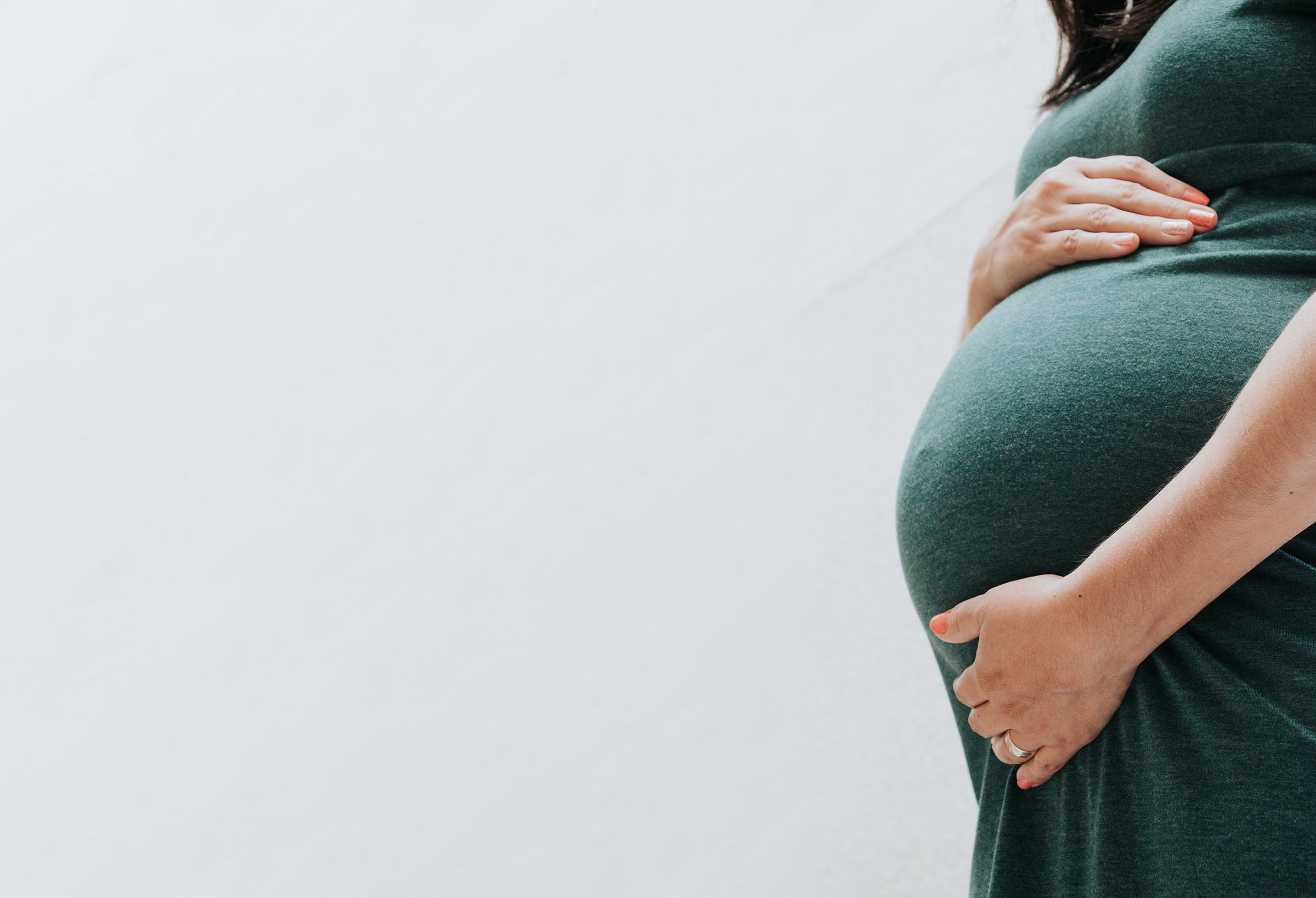 pregnant persn wearing a green dress holding their belly